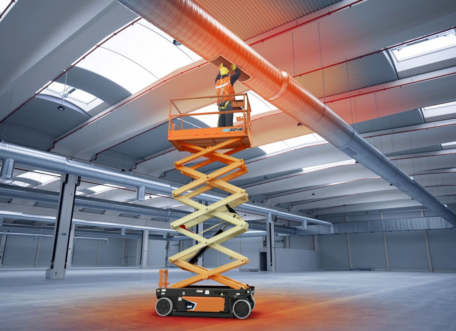 Worker stands on platform of electric scissor lift, checking overhead ductwork in large building.