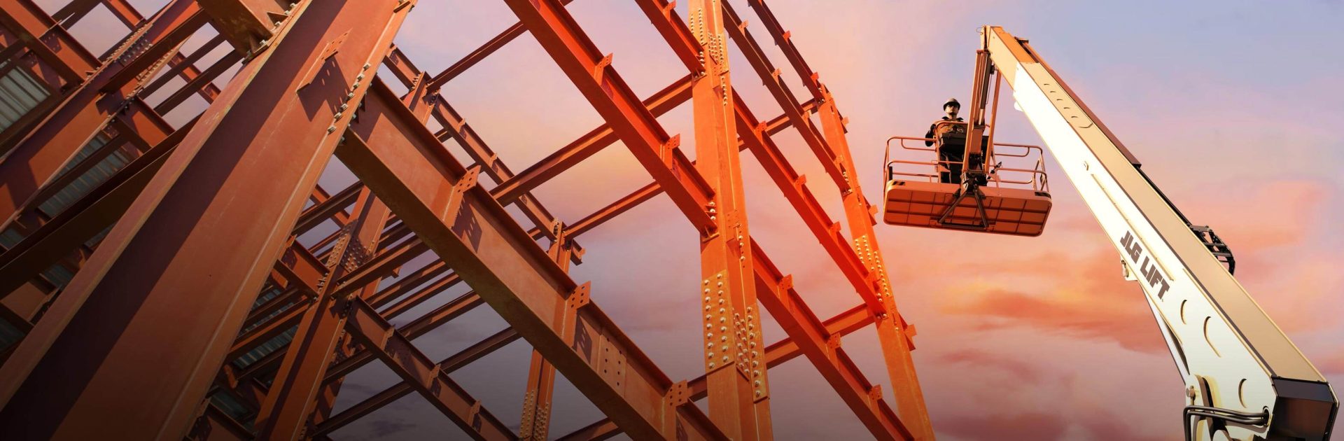 Worker stands on platform of a JLG boom lift next to structural steel frame.